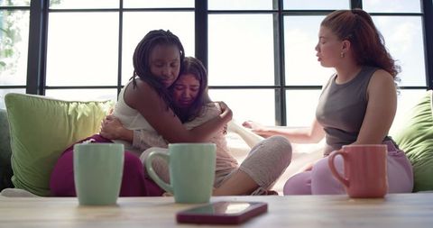 African american friends comforting crying woman on couch hugging offering support