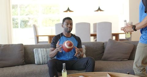 Friends tossing football on couch after pizza night, casual home recreation and sports