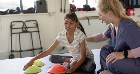 Pediatric therapist guiding child reaching for cones during motor skills activity