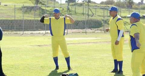 Baseball teammates stretching and chatting on sunny field in yellow and blue uniforms