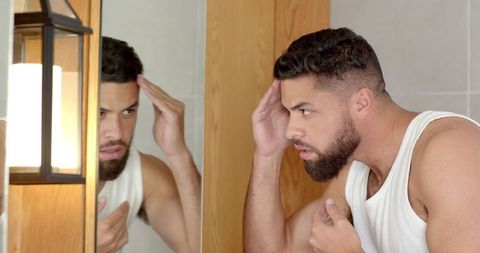 Man grooming in modern bathroom reflected in mirror