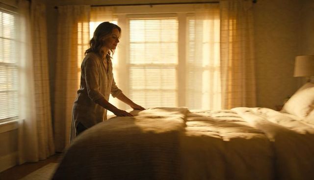 Woman smoothing duvet in sunlit bedroom during serene morning routine, warm cozy interior