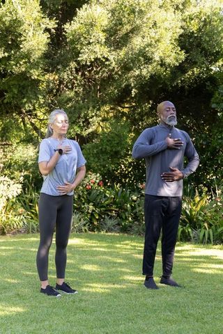 Mature diverse couple practicing mindful breathing and meditation in sunlit garden