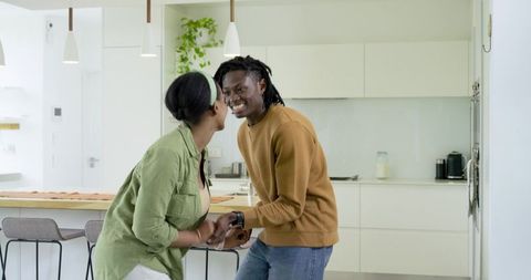 African American couple holding hands and leaning toward each other in modern kitchen