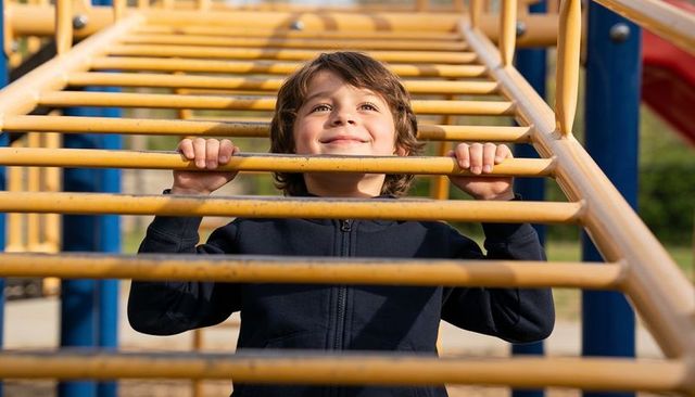 Smiling boy climbing yellow monkey bars gripping rungs outdoors on sunny playground