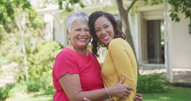 Elderly mother and young daughter hugging in garden, smiling at camera. Ideal for use in family, parenting, and relationships-themed promotions. Demonstrates joy, love, and unity in a natural outdoor environment. Suitable for advertisements, blog posts, and social media content about family bonds and spending quality time together.