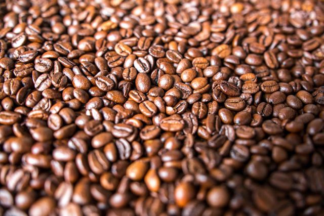 Image showing a close-up view of brown roasted coffee beans. Useful for websites, blogs, and promotional materials related to coffee shops, beverage brands, and cafes. May also serve as a background or texture in design projects.