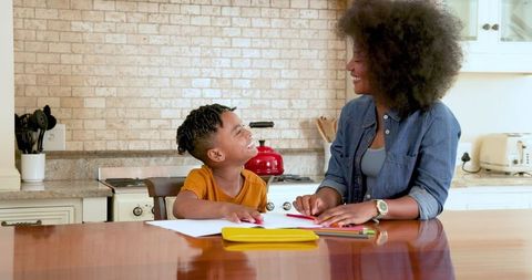 Mother Guiding Young Son with Homework at Kitchen Table