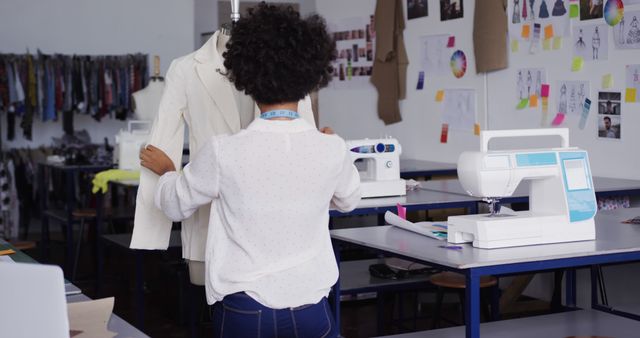 Fashion designer working on a custom garment in a studio. In a creative environment filled with sewing machines, sketches, and fabrics, the designer is seen adjusting a white jacket on a mannequin. Ideal for articles or advertisements related to fashion design, tailoring, creative workspaces, and the garment industry.