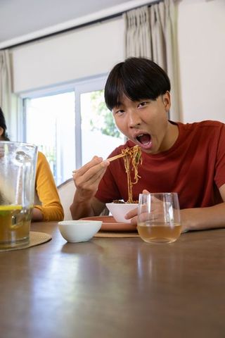 Young man enjoying noodles with friends in home dining room