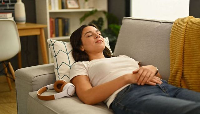 Young woman relaxing on sofa with headphones beside her, cozy living room calm moment