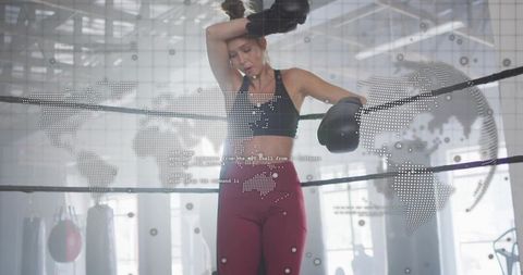 Female boxer leaning wiping forehead in industrial gym ring with dotted world map overlay