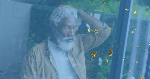 Pensive senior man contemplating by window with gold star reflections