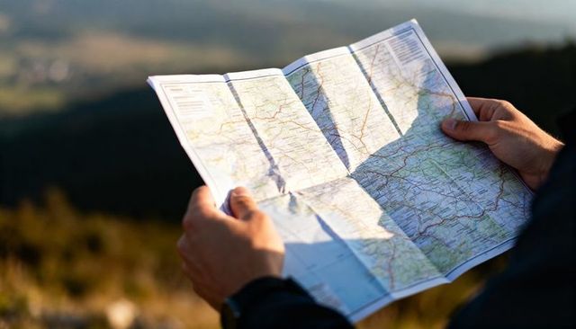 Hiker holding folded map navigating hillside at golden hour