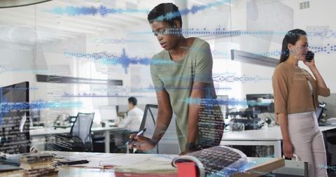 Junior professional reviewing plans with digital waveform overlay in collaborative office