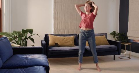 Young woman stretching barefoot in bright modern living room with navy sofa and plants