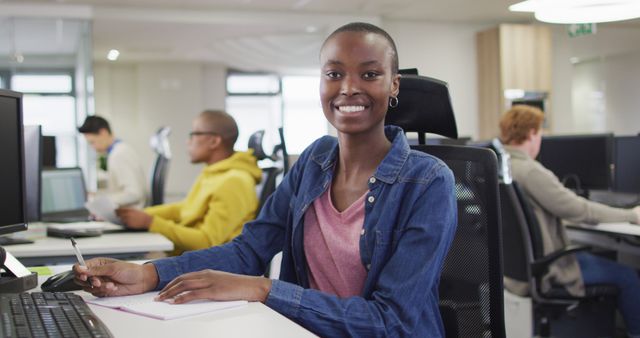 African american woman sitting at desk and working, turning and smiling at camera in office. business, teamwork and office workplace.