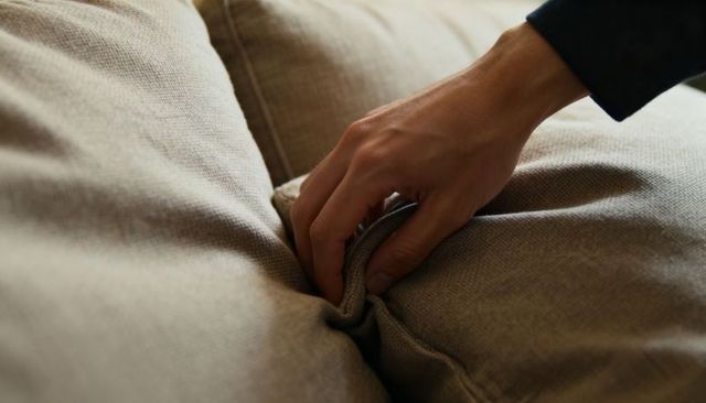 Hand adjusting beige sofa cushion close-up showing fabric texture and comfort