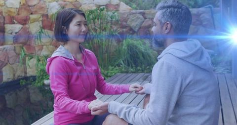 Couple holding hands meditating on wood deck by pond with sunlit blue lens flare