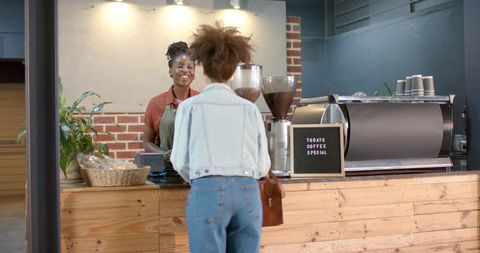Smiling barista serving customer at coffee counter with espresso machine and pastries
