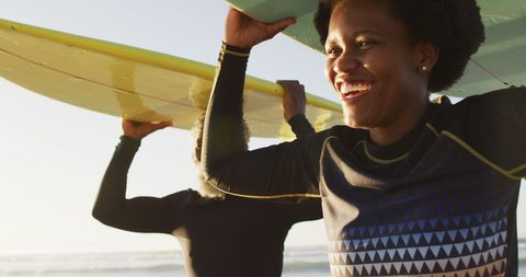 Happy african american couple walking with surfboards on sunny beach. healthy and active time beach holiday.