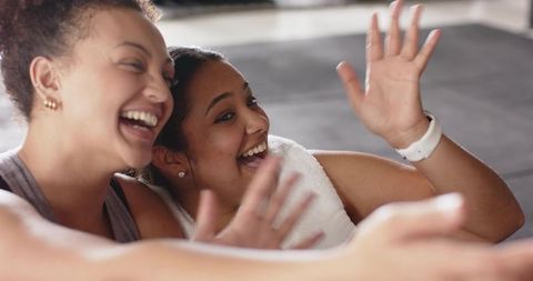 Female friends laughing and leaning together after gym workout, candid fitness moment