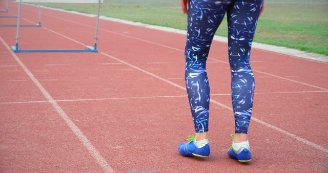 A person stands on a track field ready to run, showcasing athletic footwear and sportswear. Their stance suggests preparation for a sprint or workout, emphasizing the importance of physical fitness and active lifestyle.