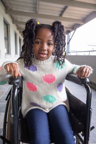 Smiling Girl with Polka Dot Sweater Navigating Wheelchair Outdoors