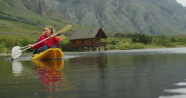 Couple kayaking on scenic mountain lake. Man and woman paddling yellow kayak in tranquil waters near a rustic cabin. Perfect for outdoor adventure, travel, and vacation-related uses. Highlights active lifestyle, natural beauty, and recreational sports.