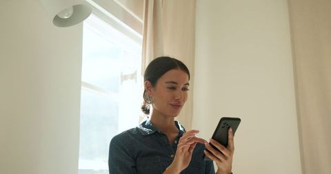 Woman Engaging With Her Smartphone Under Natural Light at Home