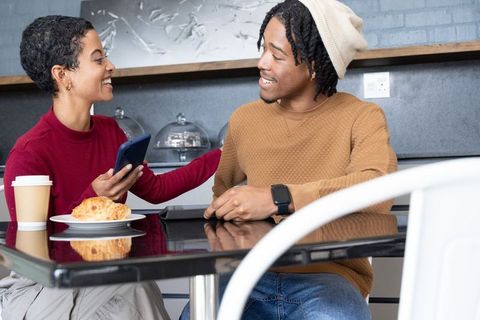 Smiling african american couple sharing coffee and pastry while showing smartphone