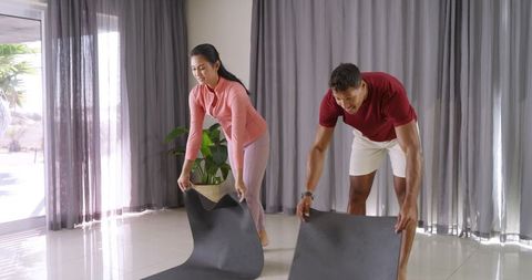 Couple unrolling yoga mats in sunlit living room preparing for home workout