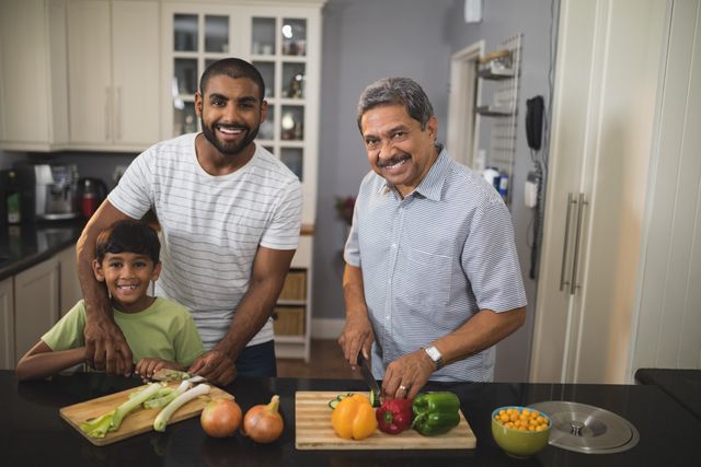 Multi-generation family enjoying time together in kitchen while preparing food. Grandfather, father, and son smiling and bonding over cooking. Ideal for concepts related to family time, healthy eating, and domestic life.