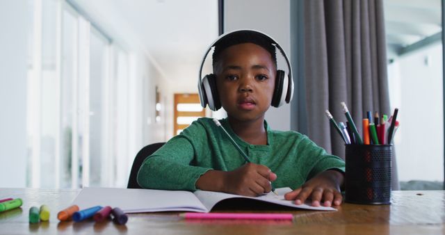 Portrait of african american boy waving and doing homework looking at the camera. distant learning and online education concept