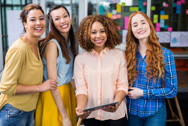 This image depicts a group of diverse female executives collaborating and discussing ideas using a digital tablet in a modern office environment. They are smiling and appear engaged, suggesting a positive and productive work atmosphere. This image is ideal for use in business-related content, articles on workplace diversity, teamwork, and technology in the office. It can also be used for promoting professional development programs, corporate culture, and women's leadership initiatives.