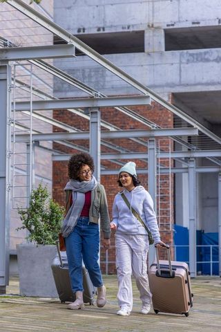 African american and asian women walking with luggage through urban plaza