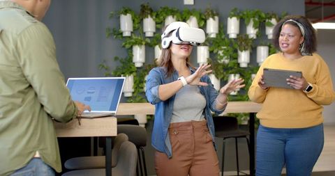 Diverse coworkers testing virtual reality headset collaborating on design in modern office