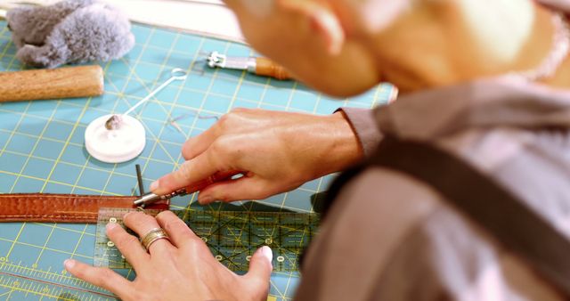 Person using precise cutting tools to craft a leather belt. Ideal for illustrating traditional craftsmanship, DIY projects, artisanal work, and hobby crafting. Can be used in content related to handmade leather goods, skill development, or artisan profiles.