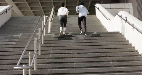 Diverse pair running up urban concrete stairs in hoodies training on outdoor granite steps