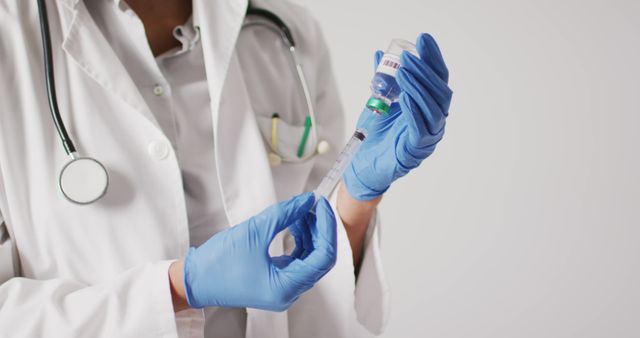 Doctor in white lab coat preparing syringe with medicine. Hands wearing blue gloves drawing liquid from vial into syringe. Ready for medical procedure. Ideal for healthcare, medical, hospital promotions and educational materials.