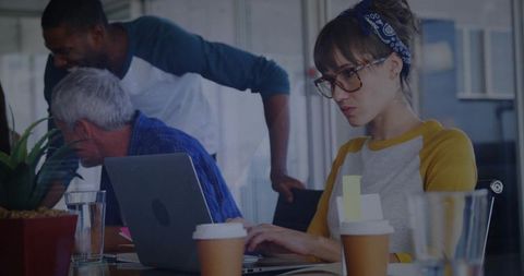 Focused woman typing on laptop while team collaborating around conference table with coffee