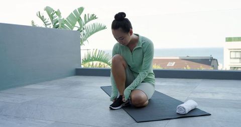 Woman Tying Running Shoes on Rooftop Yoga Mat for Outdoor Fitness