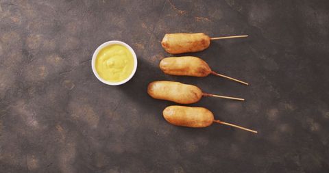 Corn dogs with mustard dip on dark background