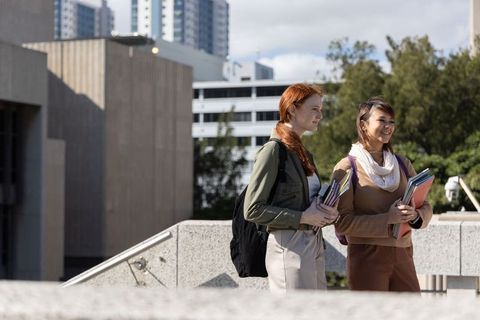 Diverse female students walking on campus carrying books and backpacks talking and smiling