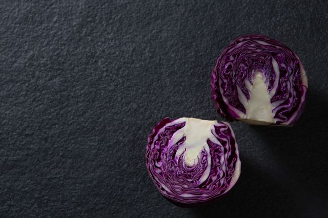 Close-up of halved red cabbage on dark slate background. Ideal for use in food blogs, cooking websites, nutrition articles, and healthy eating promotions. The vibrant purple color and intricate texture make it visually appealing for culinary presentations and recipe illustrations.