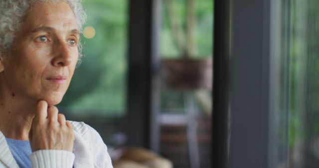 Thoughtful Senior Woman Looking Through Window with Reflective Expression - Download Free Stock Images Pikwizard.com