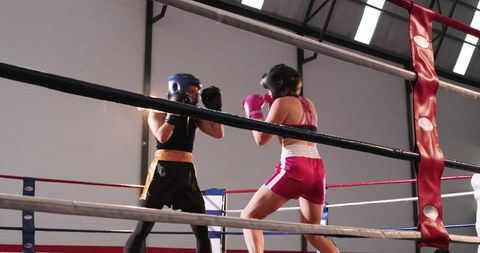 Female boxers sparring in indoor ring wearing headgear and colorful gloves during training