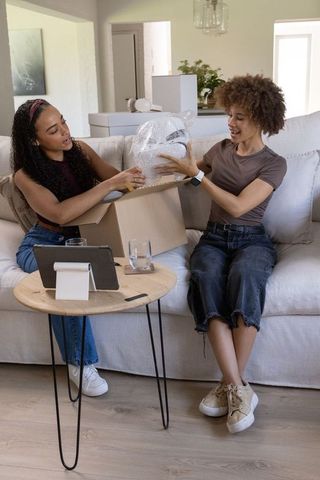 African american friends unpacking bubble-wrapped helmet on cozy living room sofa
