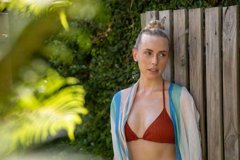 Woman in bikini top relaxing by wooden fence in garden