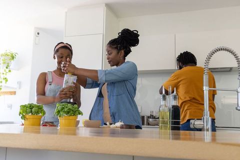 African family cooking together in bright modern kitchen, women pressing fresh basil